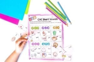 Child using short vowels phonics worksheet by gluing cutouts onto the worksheet