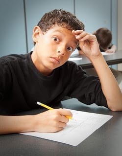 Worried student looking at camera with large eyes holding a pencil with a standardized test in front of him