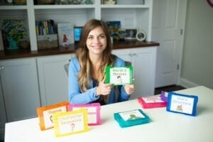 Woman holding a set of task cards in a green photo box with other reading task cards scattered on a desk in front of her.