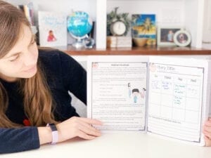 Woman holding literature journal with one page showing a story focused on character traits and another showing a student worksheet. 